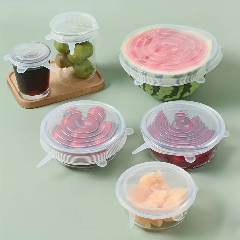 Silicone food covers on various containers including fruits and drinks on a light green background