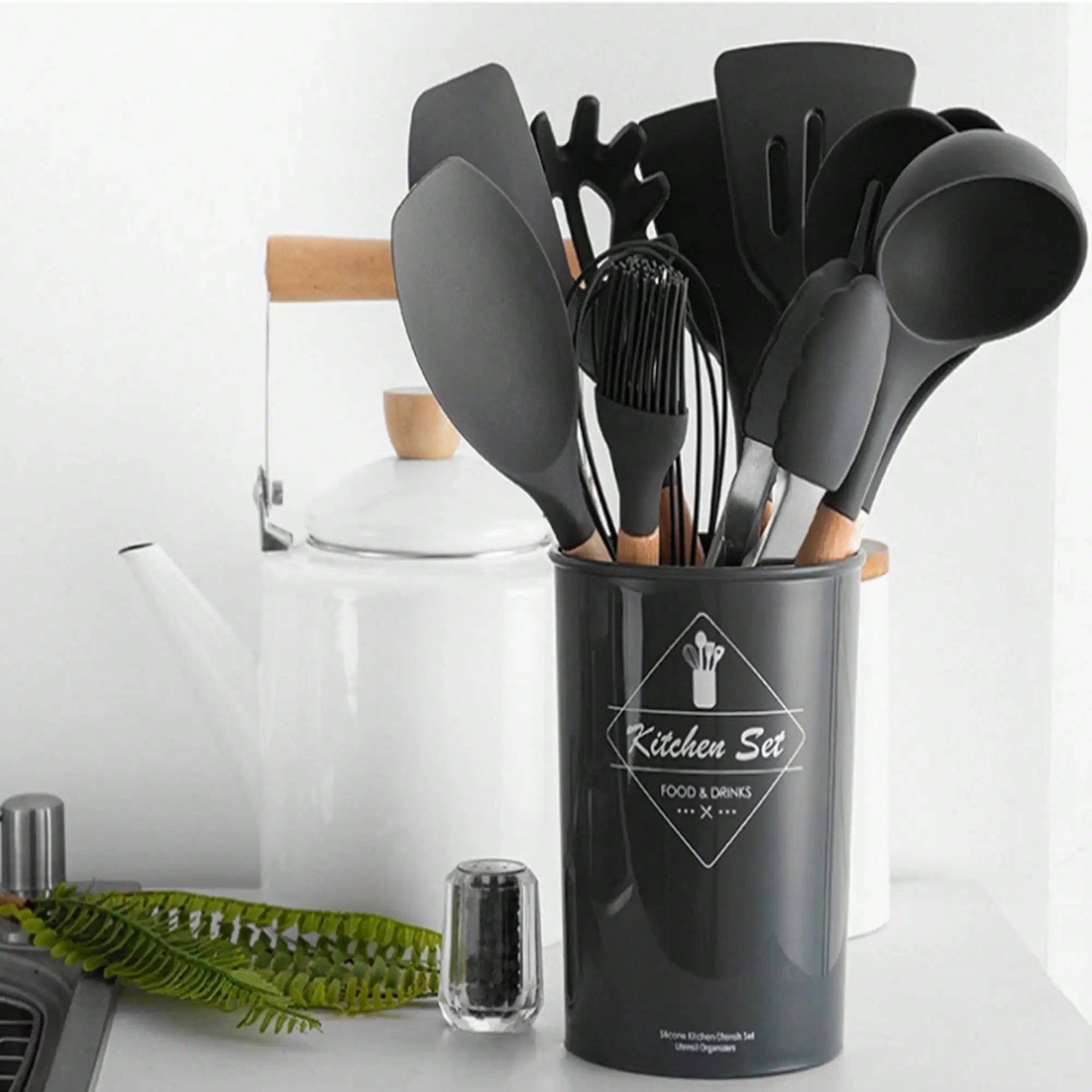 Set of kitchen utensils in a black container on a white surface with a blurred background