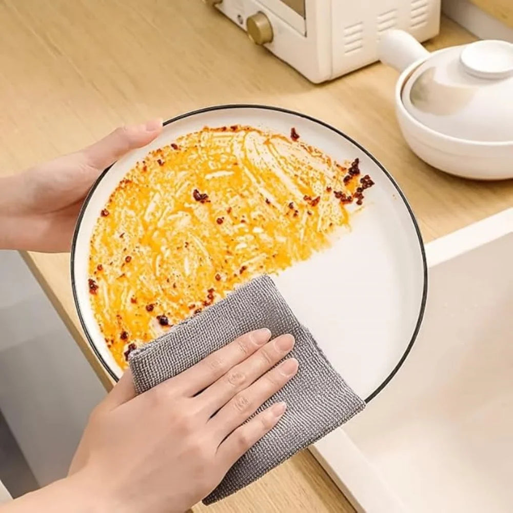 Person cleaning a plate with a gray cloth on a kitchen counter.