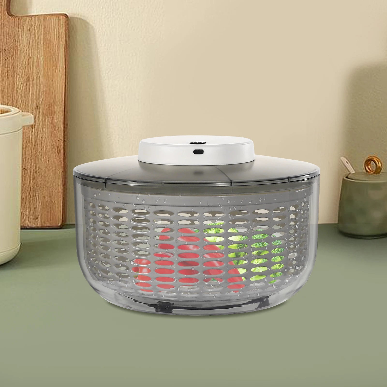 A salad spinner with a clear plastic basket, a white top lid, and a dark gray base, shown on a kitchen counter with vegetables inside.