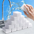 White cleaning sponges stacked on a kitchen counter with water splashing from a faucet in the background.