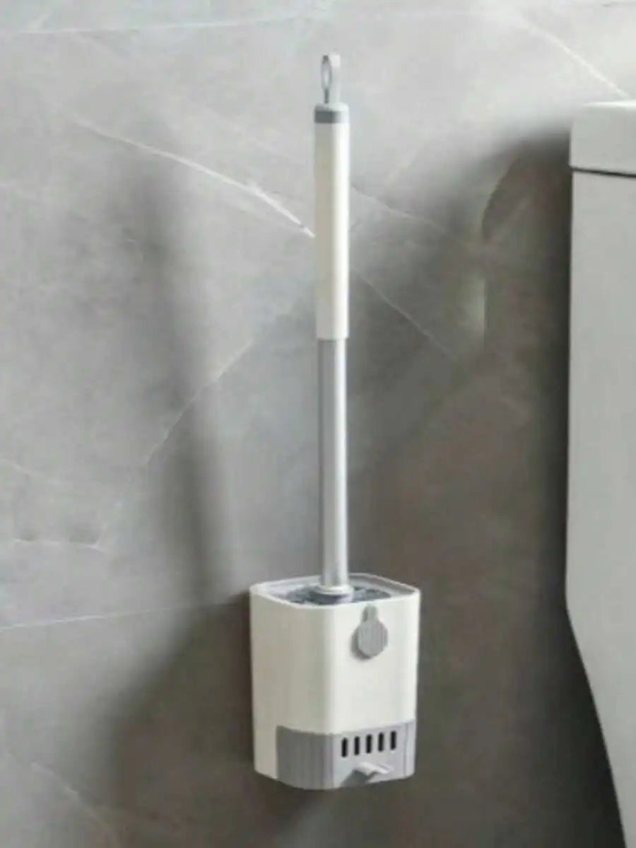 White toilet brush holder with a brush against a gray tiled wall.