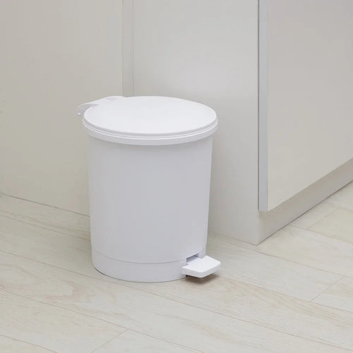 White trash bin with foot pedal on a light wooden floor.