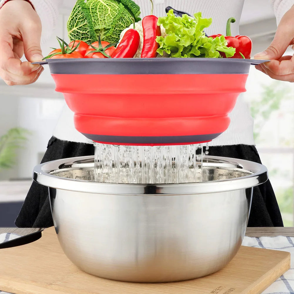 Collapsible red strainer being used to drain water from vegetables into a metal bowl.