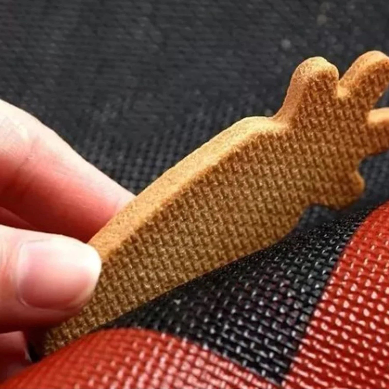 Close-up of a hand holding a brown woven strap against a textured black and red background