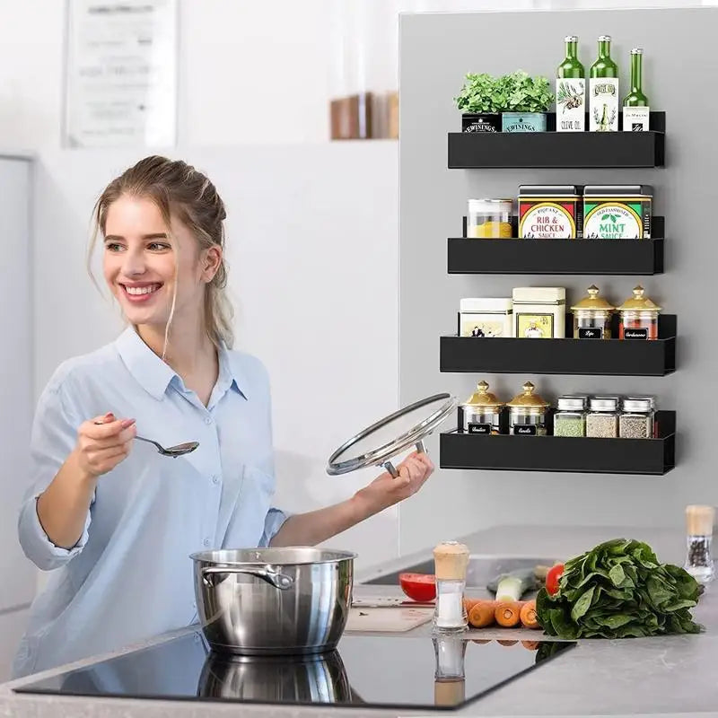 Woman in a kitchen with black wall shelves holding a pot and ladle, smiling.