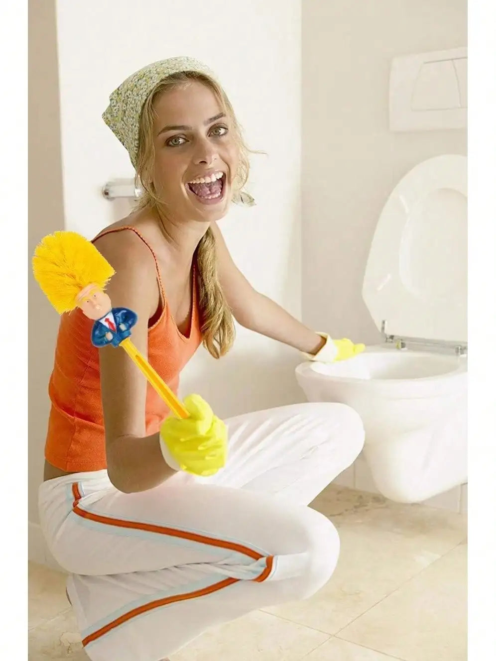 A woman in an orange tank top and white pants kneels in a bathroom holding a yellow cleaning brush near a toilet.