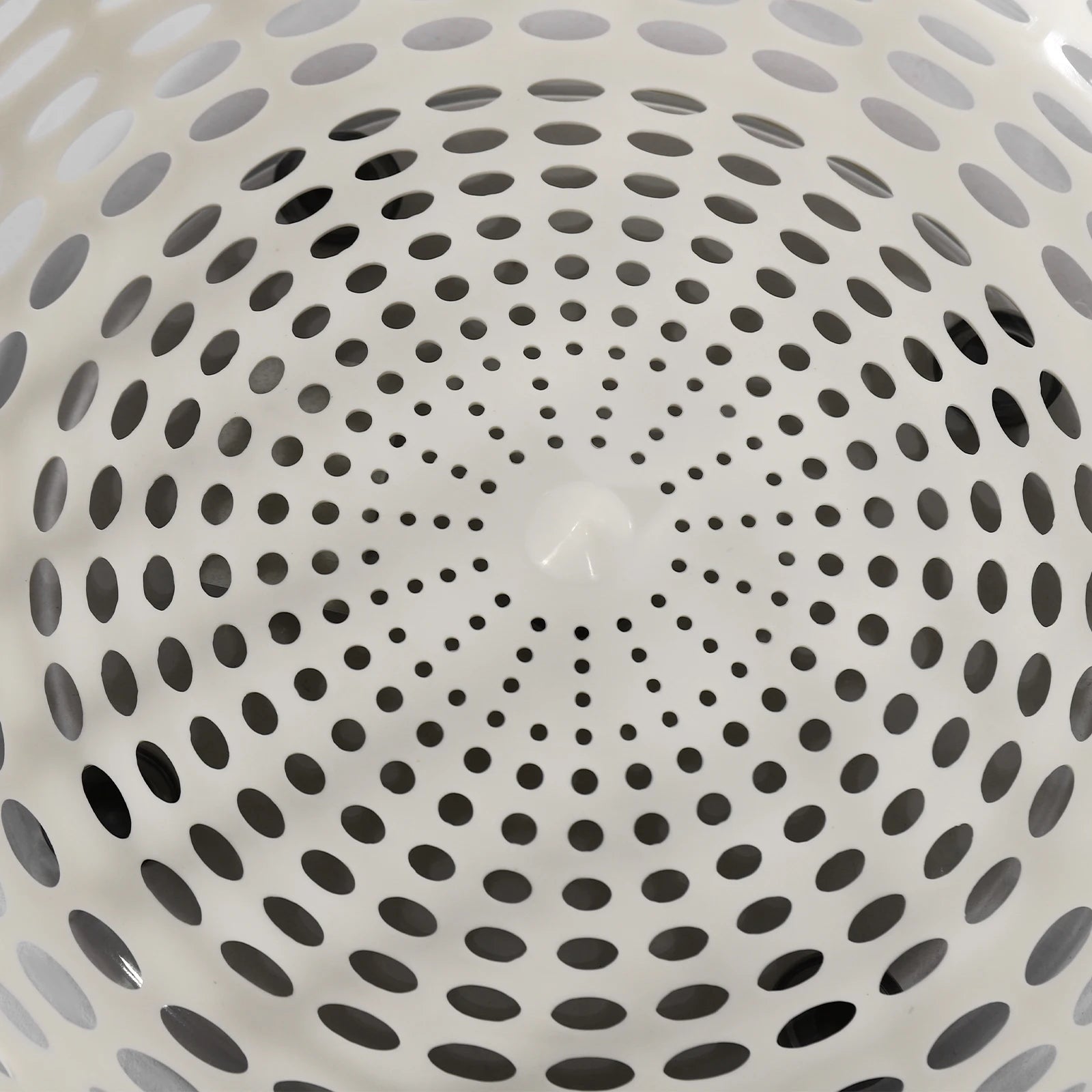 Close-up of the inside of a white plastic basket or colander with a circular pattern of perforated holes.