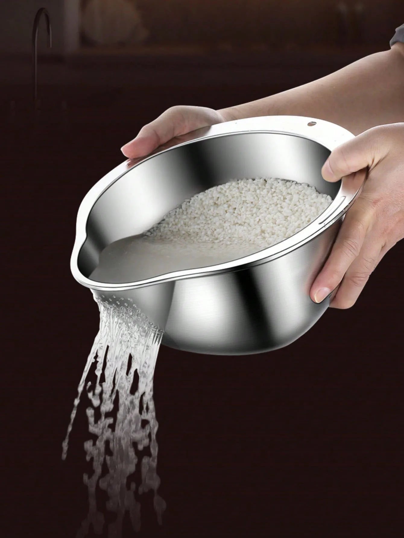 Stainless steel colander being held over a dark surface with rice spilling out.
