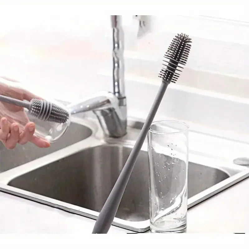 Person using a long-handled cleaning brush to clean a glass in a kitchen sink.