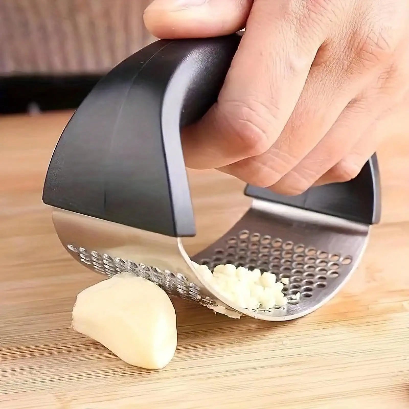 Garlic press being used to crush a garlic clove on a wooden surface