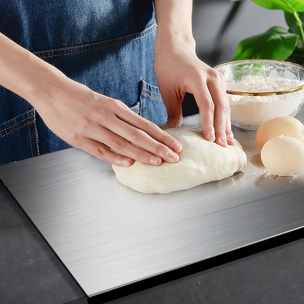 Person kneading dough on a metal surface with a bowl of flour and eggs in the background.