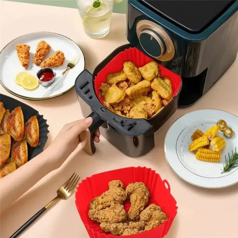 Person using a black air fryer with red silicone basket to cook food on a beige table.