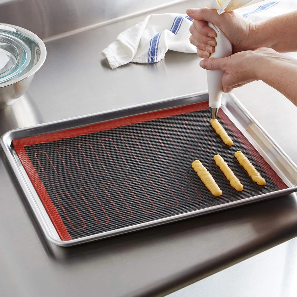 Person using a piping bag to fill pastry shapes on a silicone mat.