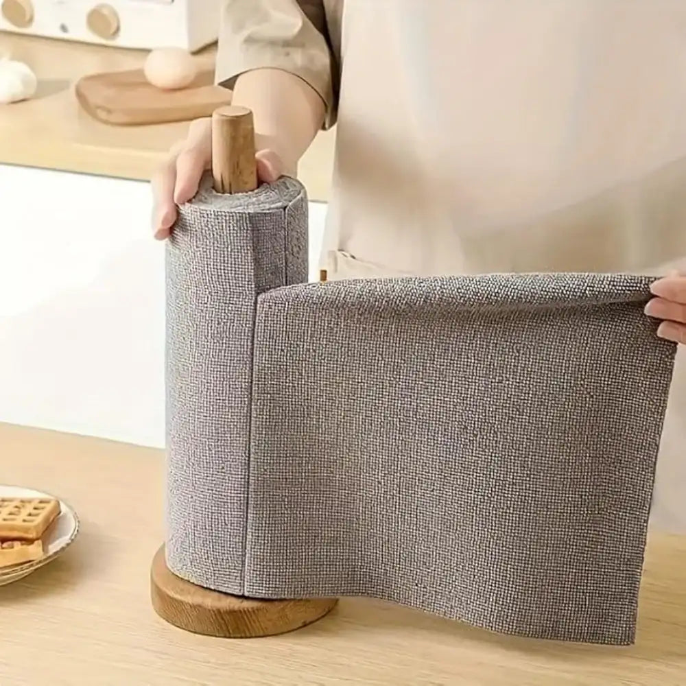Person unrolling a roll of gray fabric on a wooden surface with a blurred background