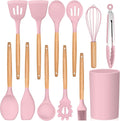 Set of pink kitchen utensils with wooden handles and a pink container on a white background