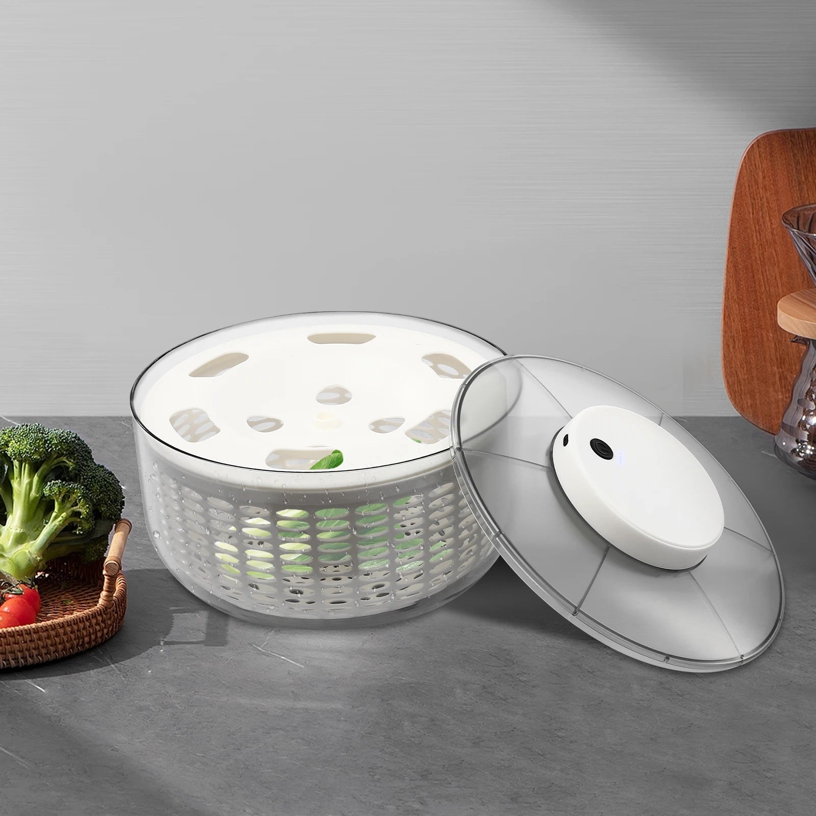 White salad spinner with a clear lid on a gray surface, surrounded by vegetables.
